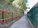Railway station pathway, fitted with red DDA disability handrails. Featuring a green safety fence to the right 